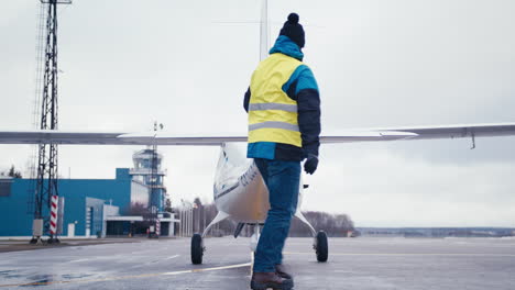 Private-aircraft-pilot-performing-preflight-external-check-of-small-white-ultralight-airplane-during-winter