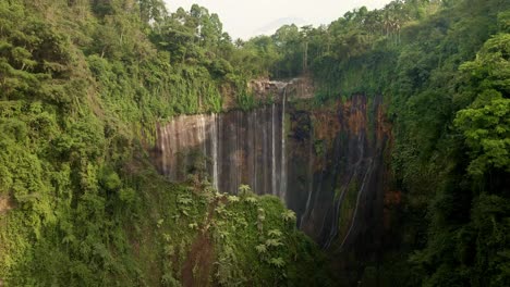 Hidden-waterfall-in-a-lush-rainforest-oasis-during-dry-seasons,-aerial-4k-drone-footage