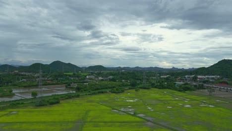 Beautiful-Scenic-Landscape-of-Paddy-Fields-and-Mountains-in-the-Background-from-an-Aerial-Drone-in-Ratchaburi-Province,-Thailand