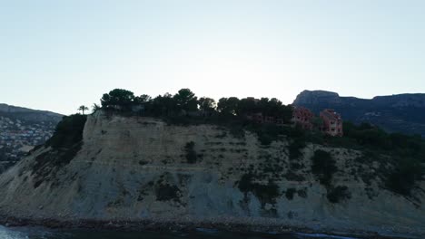 Cliffside-houses-overlooking-the-sea-during-sunset-in-Alicante,-Spain,-with-calm-waters