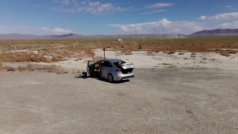 Drone-orbiting-around-vehicle-with-man-on-board-parked-in-rural-rest-area-along-highway,-Utah-state-in-USA