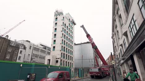 Crane-operating-at-construction-site-on-Wells-Street-off-Oxford-Street,-London,-on-a-cloudy-day