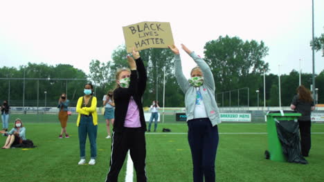 Two-young-caucasian-girls-holding-up-a-sign-during-Black-Lives-Matter-protest,-clapping-to-show-support