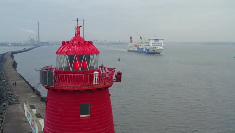 Red-lght-flickers-on-top-of-Poolbeg-lighthouse-with-cruise-ship-sailing,-Dublin-Ireland