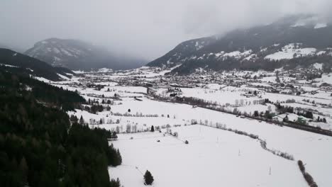 Luftaufnahme-Eines-Schneebedeckten-Feldes-Im-Nebligen-Gebirgstal-Mit-Wald-Am-Hang