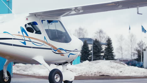 Pequeño-Avión-Ultraligero-En-La-Plataforma-Del-Aeropuerto-Con-El-Motor-En-Marcha-Y-Nieve-En-Segundo-Plano.