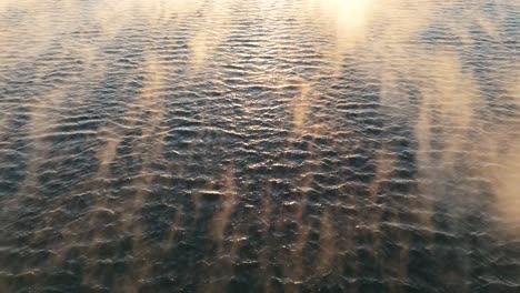 Vuelo-Aéreo-Bajo-Sobre-Olas-Con-Niebla-Flotante,-Inclinado-Hacia-Arriba-Para-Revelar-La-Puesta-De-Sol-De-La-Hora-Dorada-Cerca-De-Bjorvika,-Tiro-Ascendente