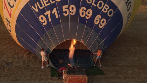 Young-couple-filling-hot-air-balloon-with-gas-flame-rising-aerial-view-watching-them-preparing-for-ride