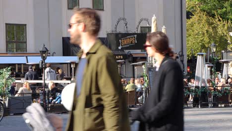 People-at-outdoor-bar-in-corona-times-in-Stockholm,-child-with-scooter-passes