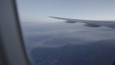 Calm-view-from-airplane-window-showing-wing-over-landscape,-blue-hues