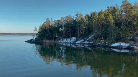 Calm-waters-of-Stockholm-archipelago-with-pine-trees-and-snow-patches,-serene-nature-scene