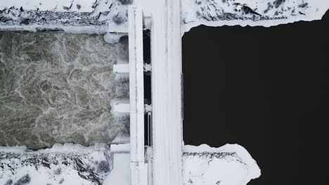 Vista-Aérea-De-Drones-Agua-Corriendo-Notigi-Estructura-De-Control-Hidropresa-Río-Lago-Paisaje-Nevado-Norte-Invierno-Manitoba-Canadá