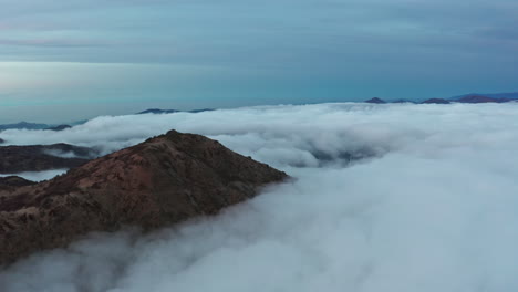 Majestic-mountain-peaks-emerging-from-a-sea-of-clouds-during-twilight,-aerial-view