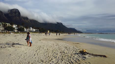 Two-women-walk-on-Camp's-Bay-Beach-as-small-dogs-run-around-them