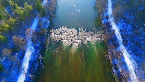 Toma-Aérea-De-Un-Río-Sereno-Que-Serpentea-A-Través-De-Bosques-Nevados-De-Invierno