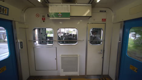 From-the-window-of-a-train-in-Fujikawaguchiko,-we-observe-blue-doors-lining-the-sides,-while-inside,-the-conductor,-clad-in-uniform,-attentively-guides-the-train-forward