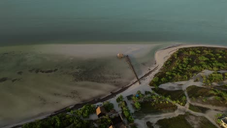 Playa-De-La-Isla-De-Holbox-Con-Aguas-Cristalinas-Y-Vegetación-Al-Atardecer,-Vista-Aérea