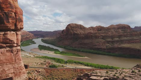 Eine-4K-Drohnenaufnahme-Von-Steilen-Klippen-Und-Einer-Eisenbahnstrecke,-Die-Entlang-Des-Colorado-River-Verläuft-Und-Durch-Die-Einzigartige-Und-Raue-Wüstenlandschaft-In-Der-Nähe-Von-Moab,-Utah,-Schneidet