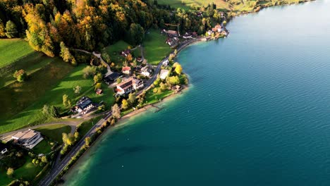 Lago-Sereno-Ubicado-En-Los-Alpes-Austriacos,-Casas-Coloridas-Salpican-La-Orilla,-La-Luz-Del-Sol-Brilla-En-El-Agua-Desde-Arriba