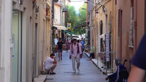 Old-man-in-sunglasses-walks-past-homeless-on-narrow-street-in-Antibes