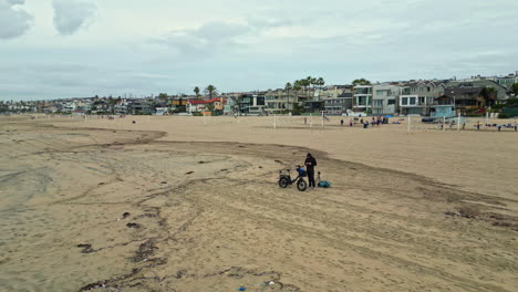 Man-flying-aerial-drone-over-empty-sand-Manhattan-beach-California-USA