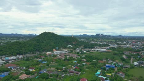 Aerial-Dolly-Shot-Over-Green-Lush-Landscape-and-Buildings-Heading-to-Khao-Kaen-Chan-Hilltop-in-Ratchaburi-Province,-Thailand