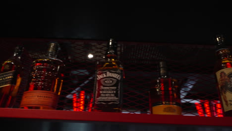 Collection-of-Whiskey-alcoholic-beverage-bottles-displayed-on-red-metal-industrial-nightclub-shelving