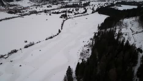 Aerial-view-of-snowy-enclosed-race-track-near-hillside-with-dark-forest