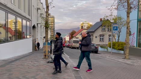 Quiet-street-scene-in-Reykjavik-with-walking-pedestrians,-parked-cars,-and-distant-mountains-at-dusk