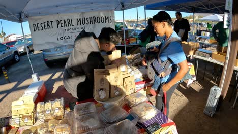 Customer-with-a-baby-in-a-front-pack-is-purchasing-fresh-mushrooms-at-a-booth-at-farmer's-market