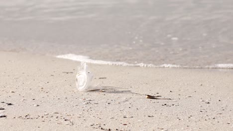 Discarded-plastic-cup-lying-on-a-sandy-beach,-waves-in-background,-environmental-issue
