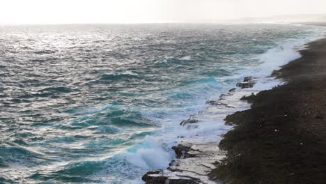 Ocean-spray-mist-rises-from-strong-ocean-waves-crashing-brilliantly-across-eroded-carbonate-rock-on-island