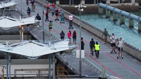 People-riding-self-balancing-scooter-and-bike,-jogging,-strolling-across-the-freshwater-reservoir-at-Marina-Barrage,-water-management-facility-in-Singapore,-irrigation,-flood-control-and-water-supply