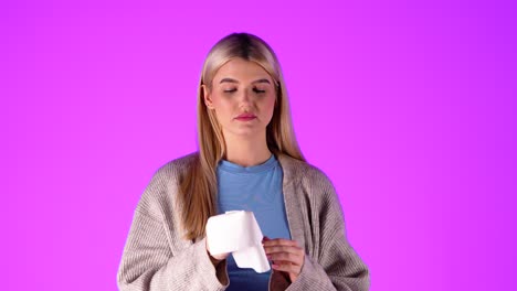Caucasian-blonde-young-woman-wipes-the-snot-nose-with-a-tissue-paper,-portrait-shot-in-studio-with-infinite-fuchsia-background