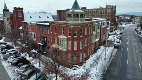 Corner-view-of-a-red-brick-building-with-a-turret,-snow-lined-streets,-and-parked-cars-on-a-cloudy-day