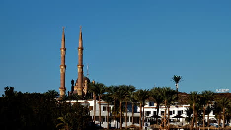 Mosque-with-twin-minarets-against-a-clear-blue-sky-in-Sharm-El-Sheikh,-Egypt,-palm-trees-surround