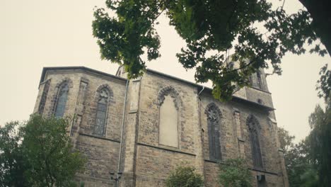 Gothic-church-surrounded-by-foliage-on-a-cloudy-day,-static-low-angle-shot