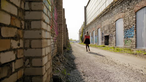 Young-blond-woman-walking-down-a-dirt-road-with-brick-walls-covered-with-artistic-murals