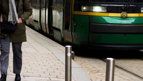 Commuters-near-green-tram-in-Helsinki-during-the-day,-dynamic-street-scene