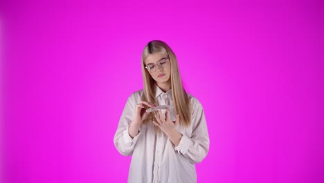 Young-White-Blonde-Lady-file-her-nails-with-Glasses-and-Sexy-Smart-Look-at-Chroma-studio-pink-background,-torso-model-woman-view