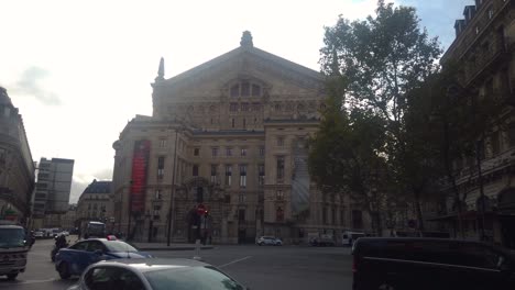 Schwenk-Des-Opernhauses-Palais-Garnier-In-Paris,-Während-Autos-Davor-Vorbeifahren