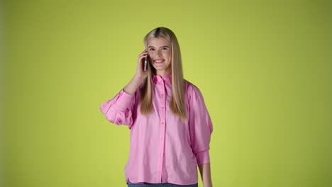 Caucasian-young-blonde-woman-talks-cheerfully-on-a-cellphone-waving-her-hands,-studio-chroma-background,-yellow-infinite-model-shot