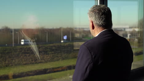 Back-view-of-an-older-businessman-looking-out-the-window-contemplating-next-deal