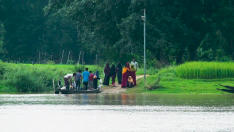 Gente-Rural-Cruzando-Un-Río-En-Un-Barco-De-Madera,-Con-Campos-Verdes-Al-Fondo