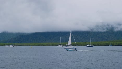 Ein-Kleines-Weißes-Segelboot-Fährt-Auf-Dem-Ruhigen-Ozean-Vorbei,-Während-Die-Besatzung-Damit-Beschäftigt-Ist,-Das-Segel-Einzuholen