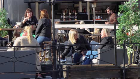 Las-Mujeres-Se-Sientan-En-Un-Bar-Al-Aire-Libre-En-Estocolmo,-Un-Hombre-Con-Máscara-Camina-En-Primer-Plano