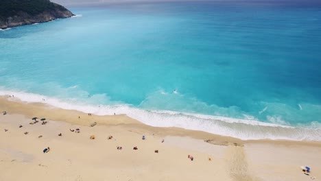 Myrtos-Strand-Auf-Kefalonia,-Mit-Türkisfarbenem-Wasser-Und-Sandstrand,-Touristen-Entspannen,-Luftaufnahme