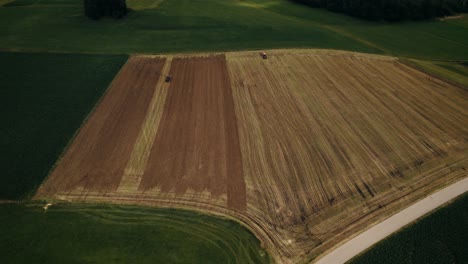 Tractors-working-in-golden-fields-with-green-boundaries,-daylight-farming,-aerial-view