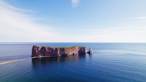 Receding-aerial-view-of-Percé-Rock-by-drone-above-the-Saint-Lawrence-River-during-a-sunny-day