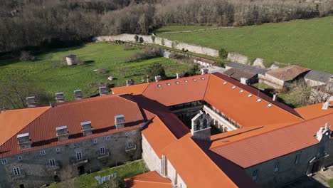 Drone-swings-back-to-showcase-orange-roof-and-chimney-brick-walls-of-monastery-in-Ourense